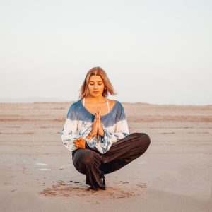 postura de yoga integral en la playa, postura del pensador con media pierna en abeja.